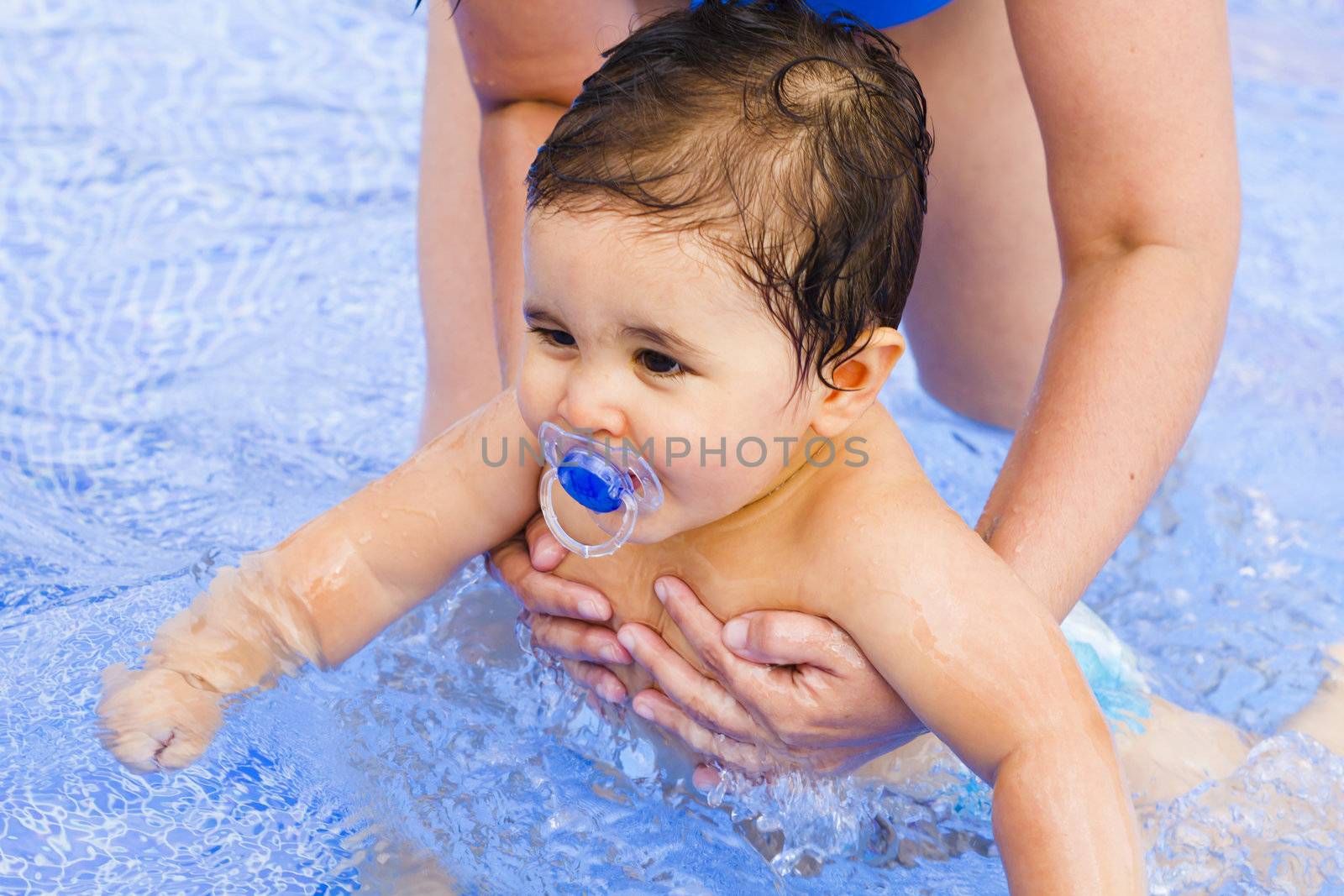 Newborn baby with a pacifier playing in the pool with his mother by FernandoCortes