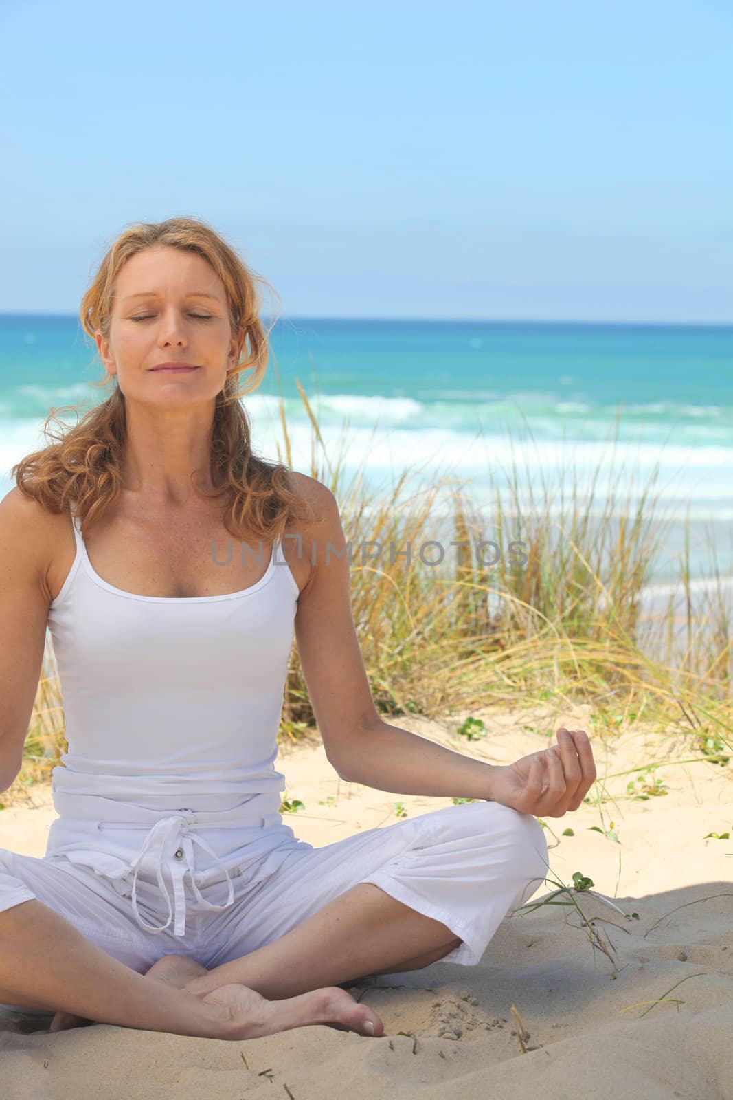 woman meditating on the beach by phovoir