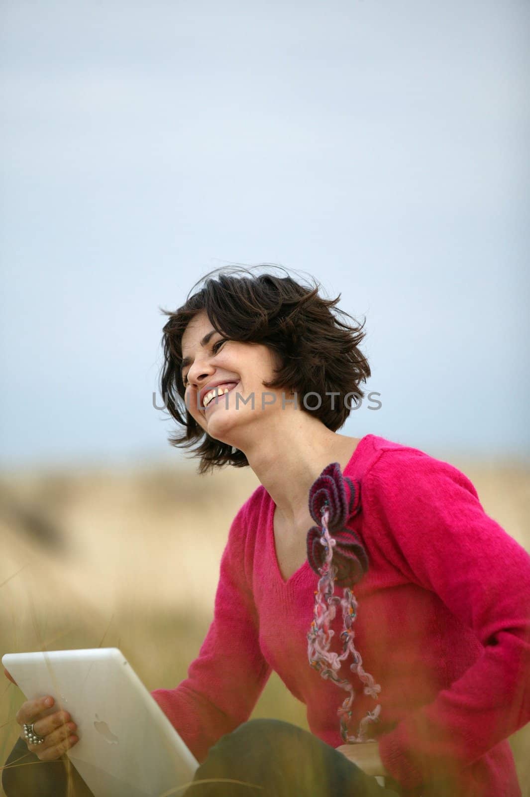 Happy brunette sat in a field with laptop