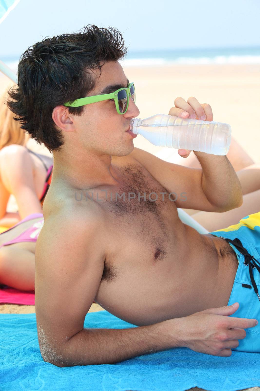 Teenager drinking water on the beach by phovoir