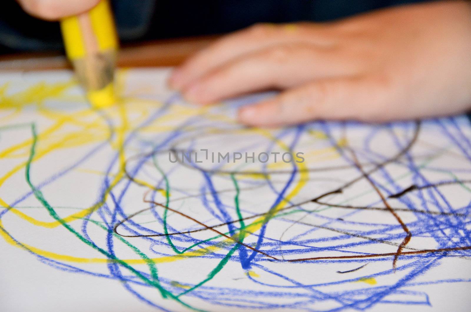 Closeup of a child drawing with yellow pen on paper