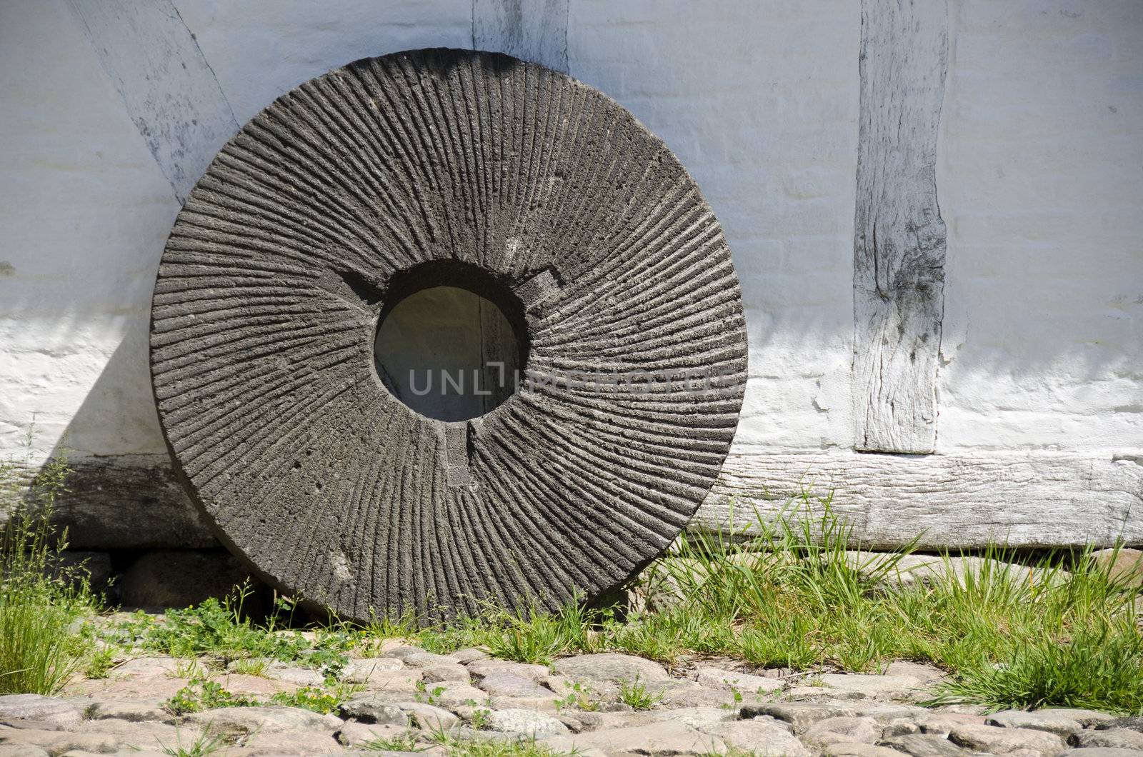 old mill stone leaning against the white wall of a traditional mill