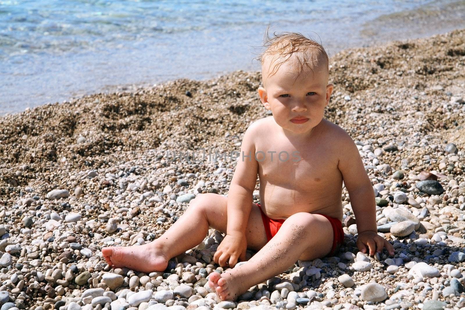 funny baby boy on beach pebble near a sea by Serp