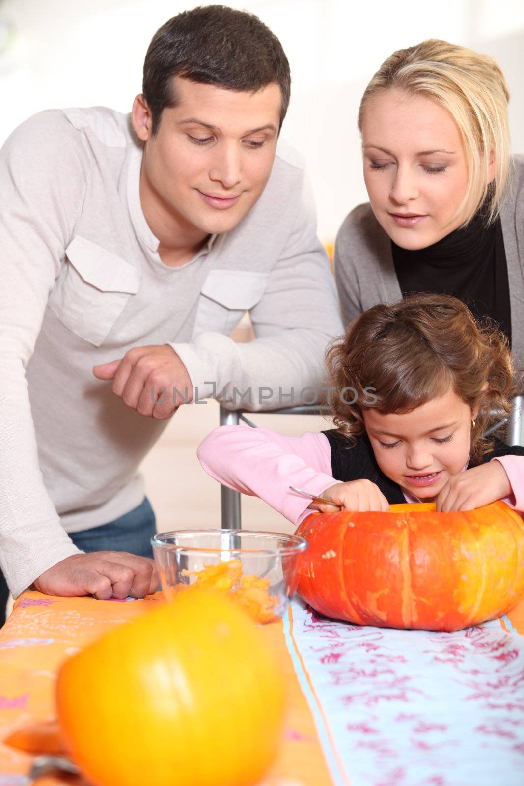 Little girl and parents carving pumpkin for Halloween by phovoir
