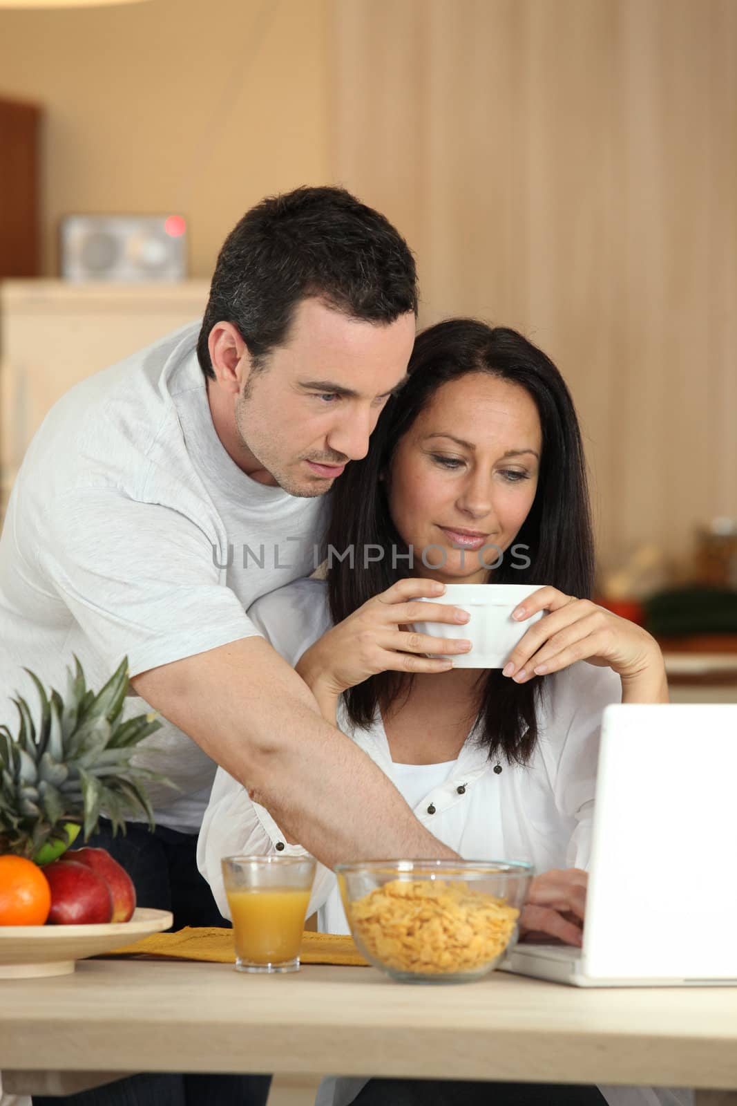 Couple eating breakfast in front of laptop by phovoir