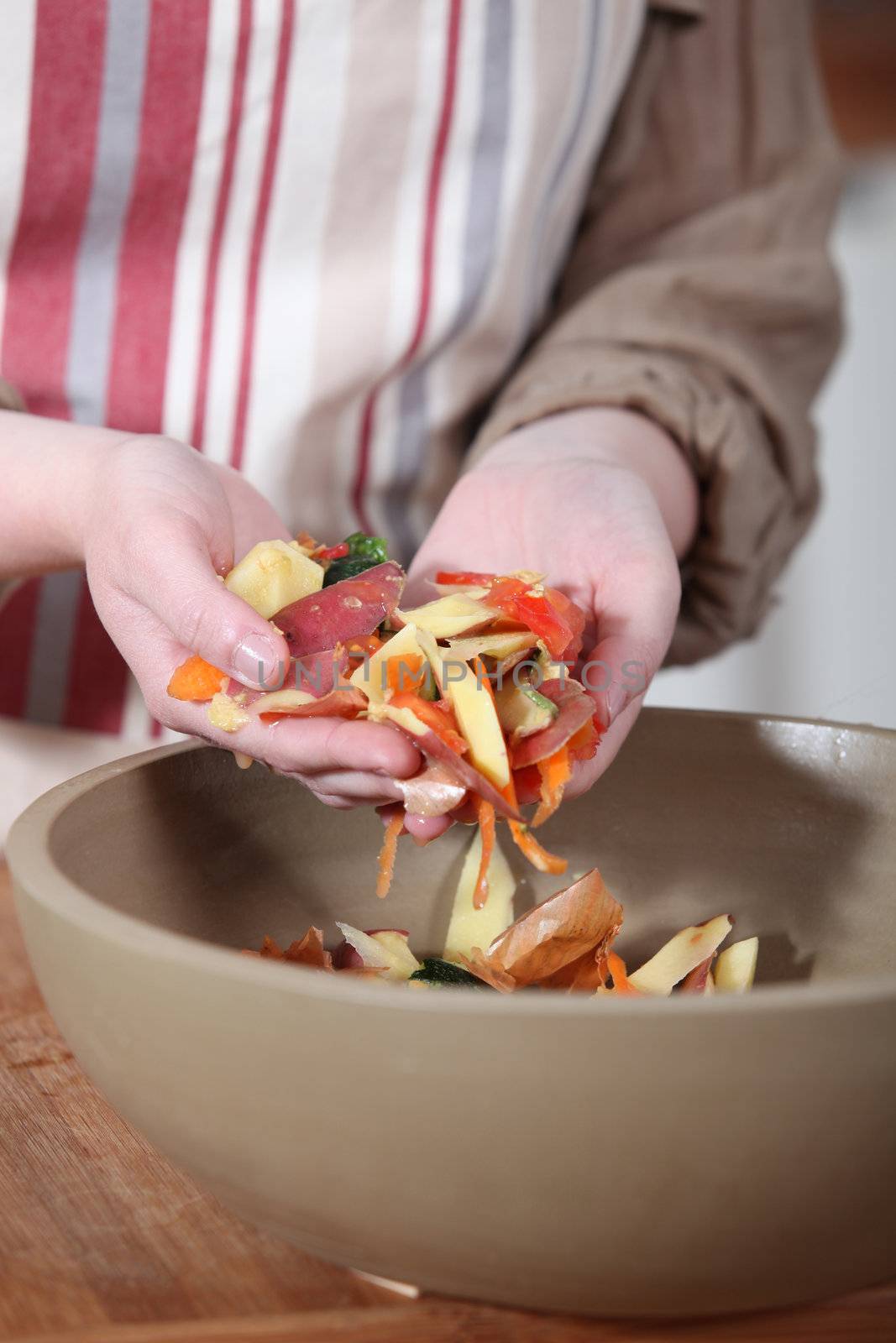 Woman gathering vegetable peeling in a bowl by phovoir