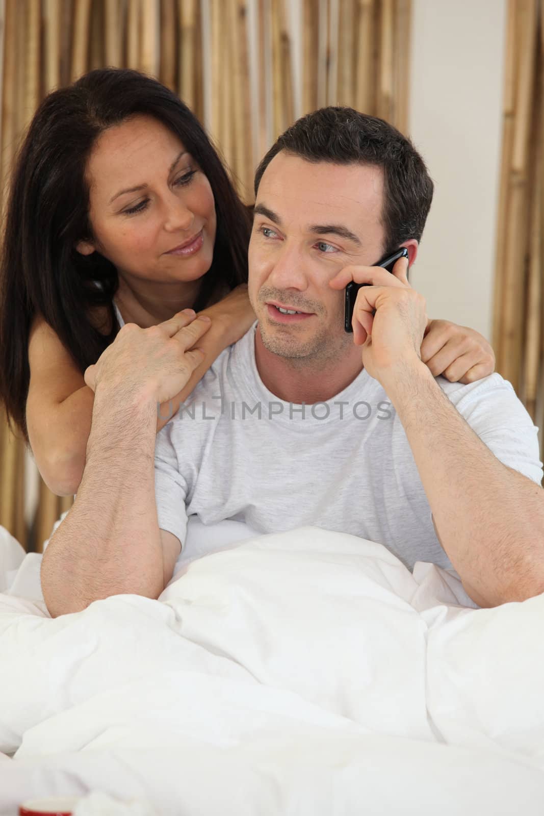 Couple making telephone call whilst in bed by phovoir