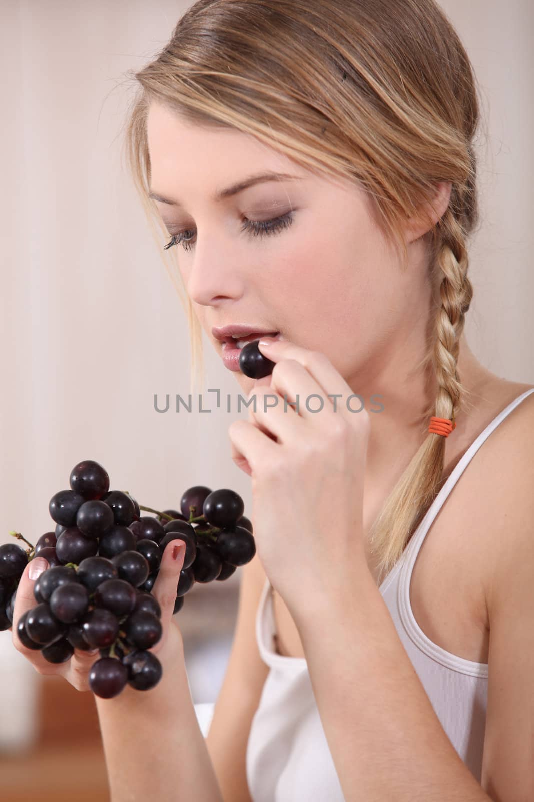 Young fair-haired woman eating grapes by phovoir