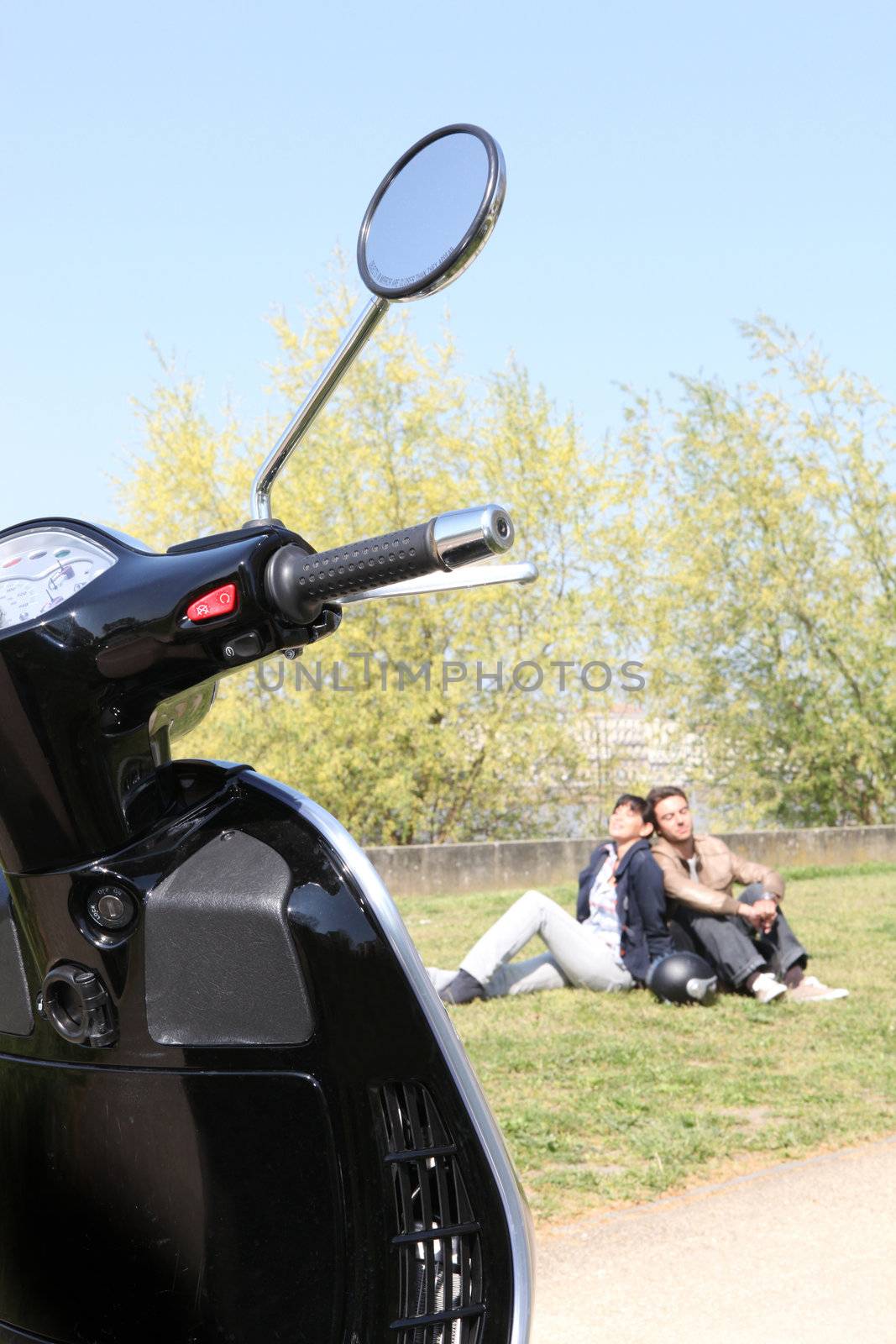Couple relaxing in a park next to their scooter by phovoir