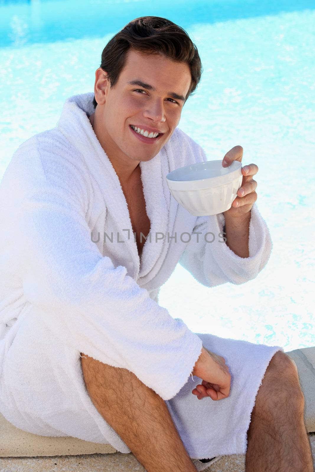young guy having coffee at edge of swimming-pool by phovoir