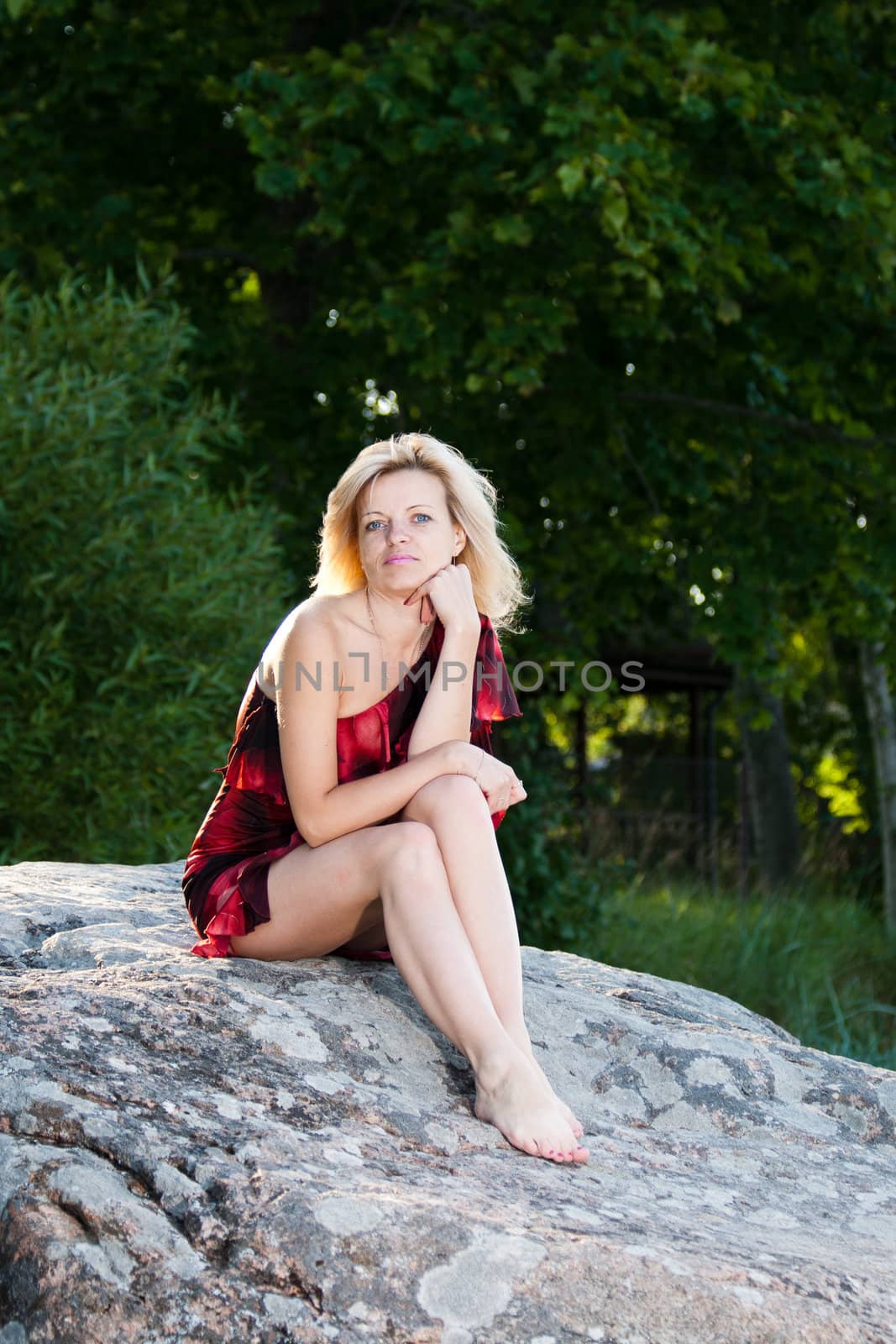 Woman sitting on a large stone with green tree leaves in the background
