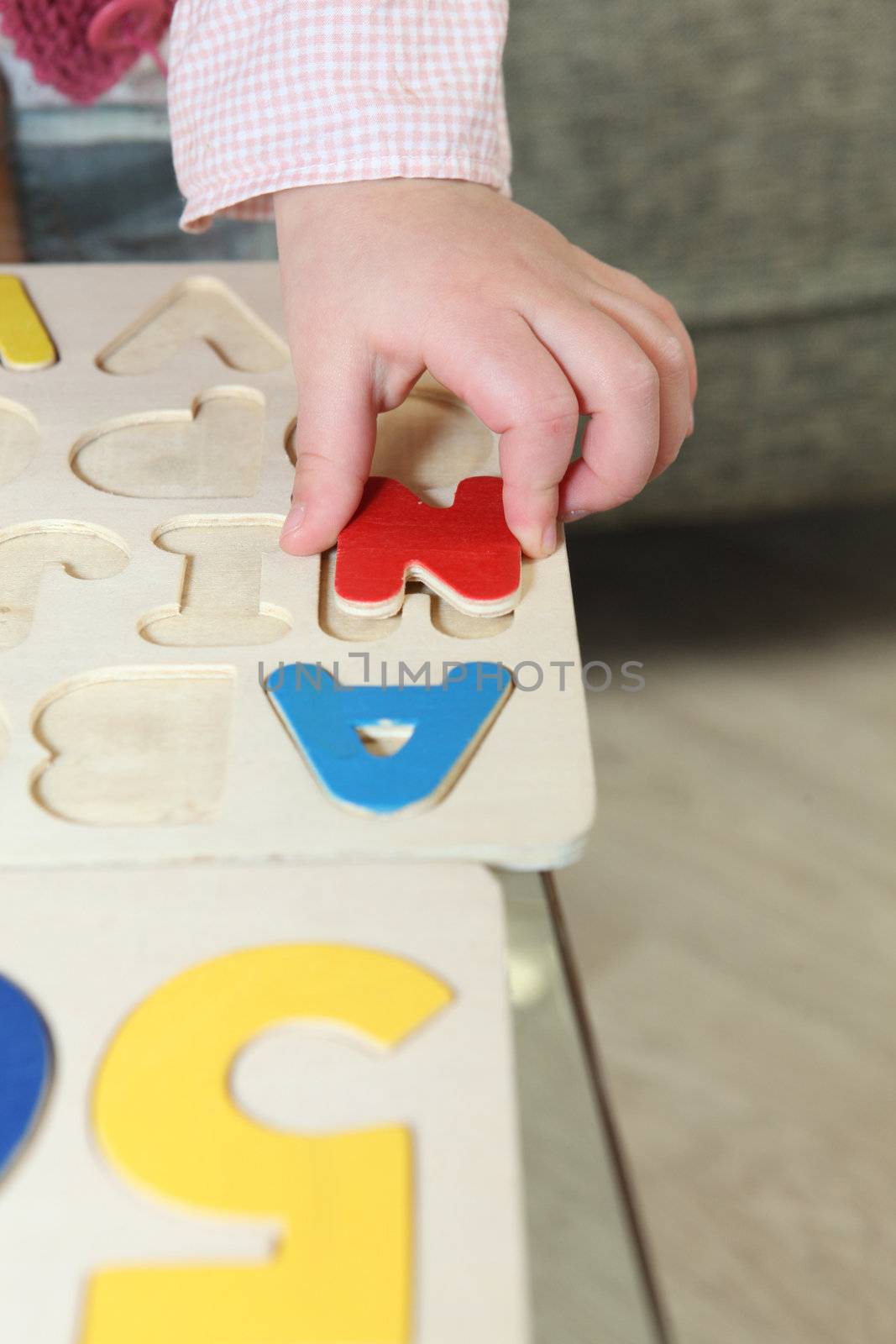Kid playing with wooden letter puzzle by phovoir