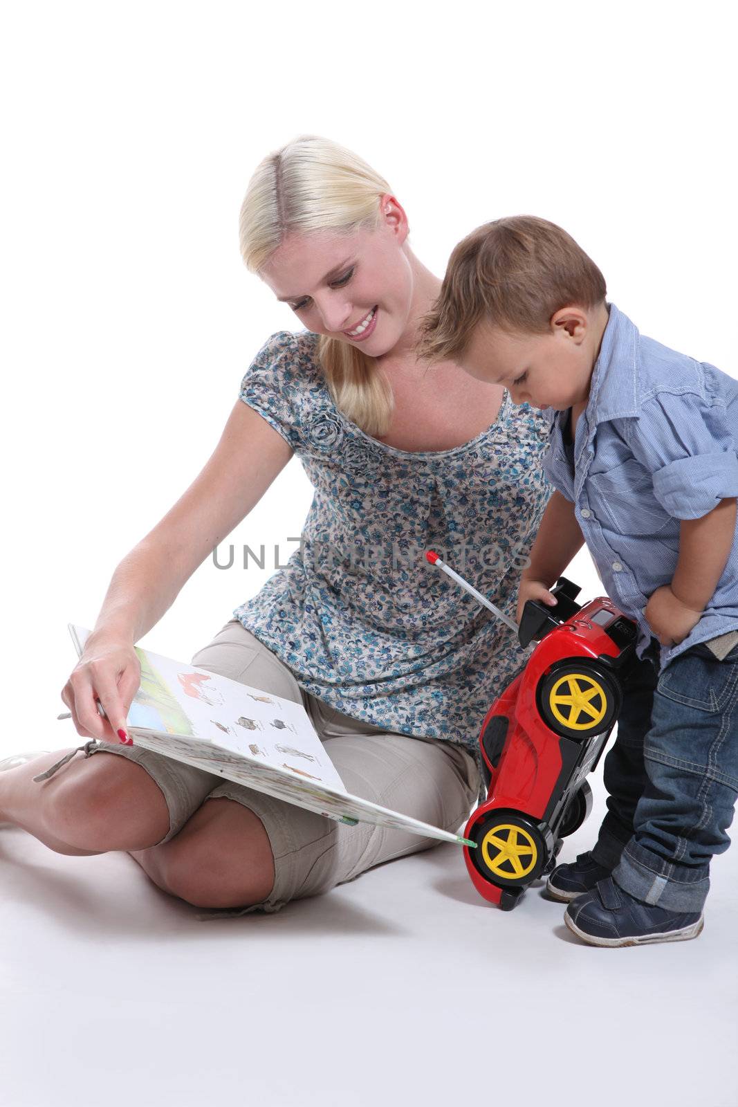 a mother showing a book to her little boy playing with a car