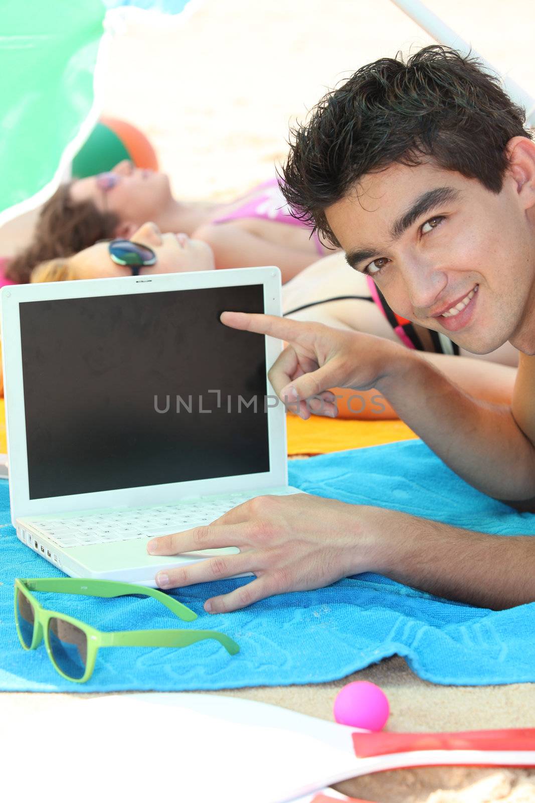 a young man on the beach showing a computer by phovoir