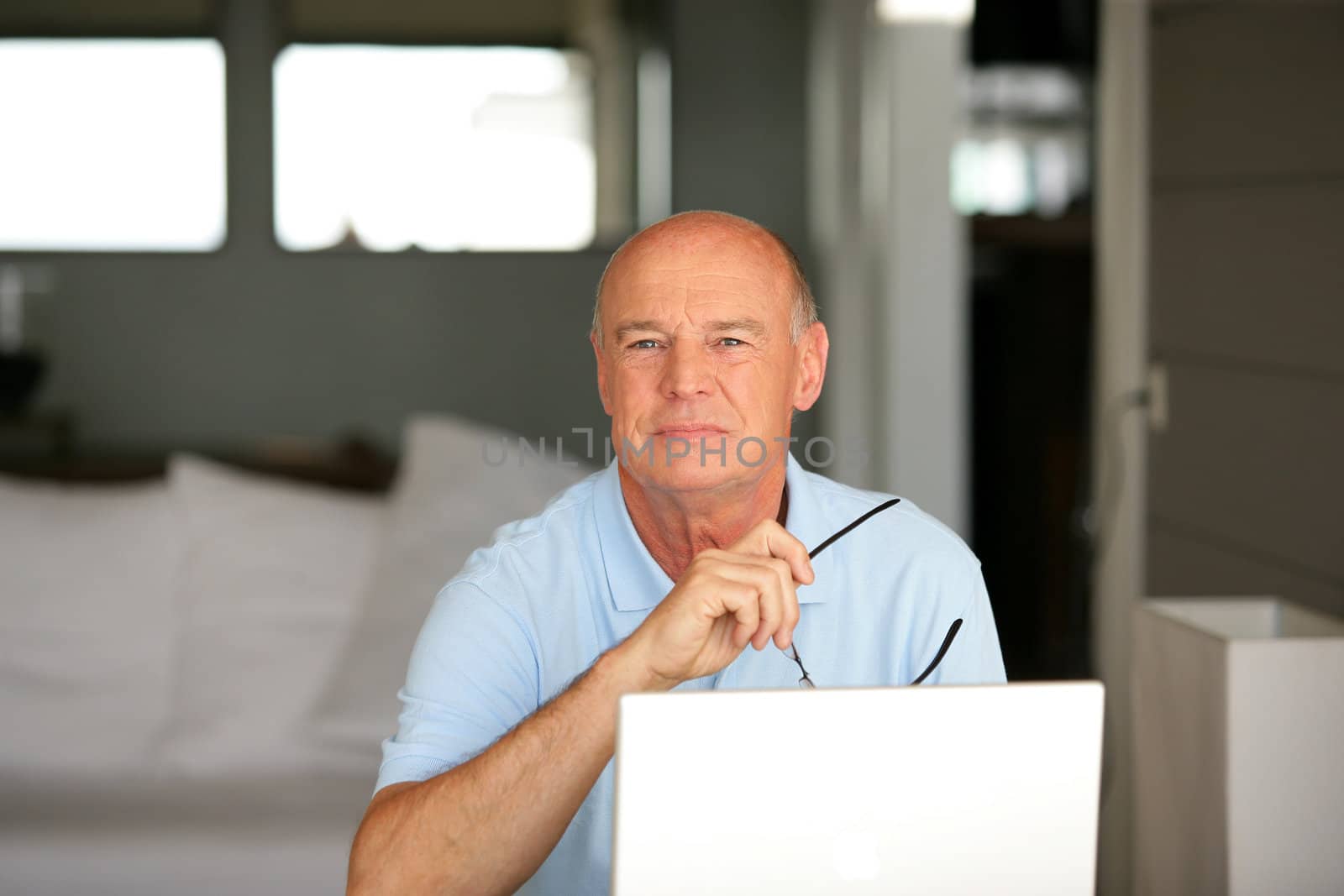 Senior man using a laptop computer at home by phovoir