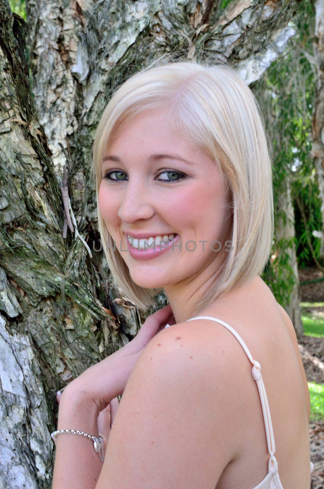 Attractive young lady with smooth features contrasting against the roughness of the paperbark tree behind her