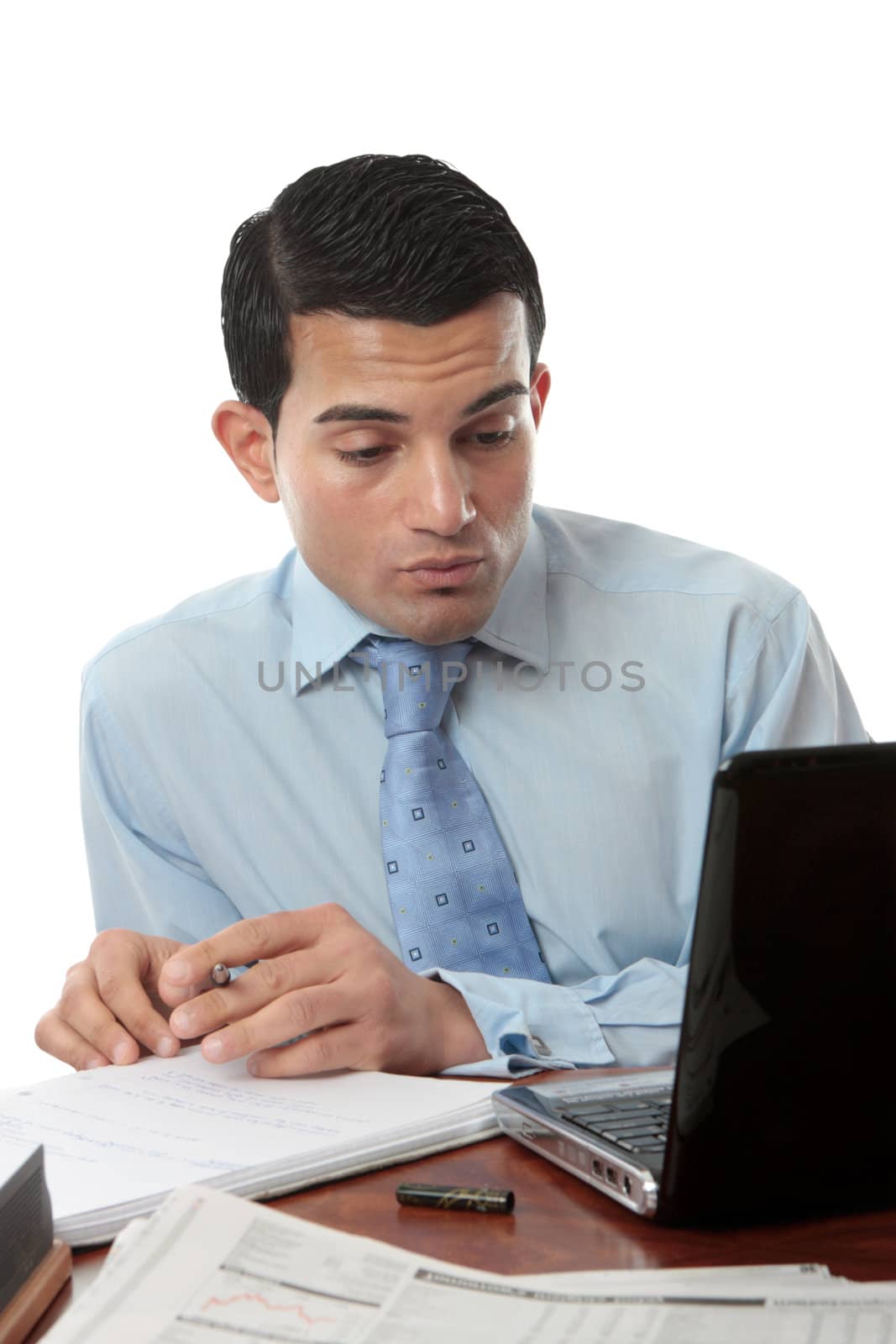 A businessman sitting at desk with paperwork, laptop and notebook working hard.