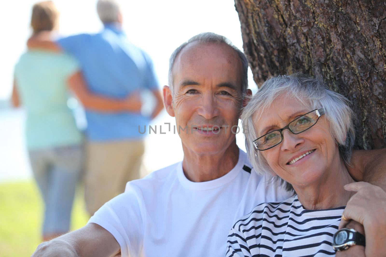 Relaxed older couple sitting in the shade of a tree on a summer's day by phovoir