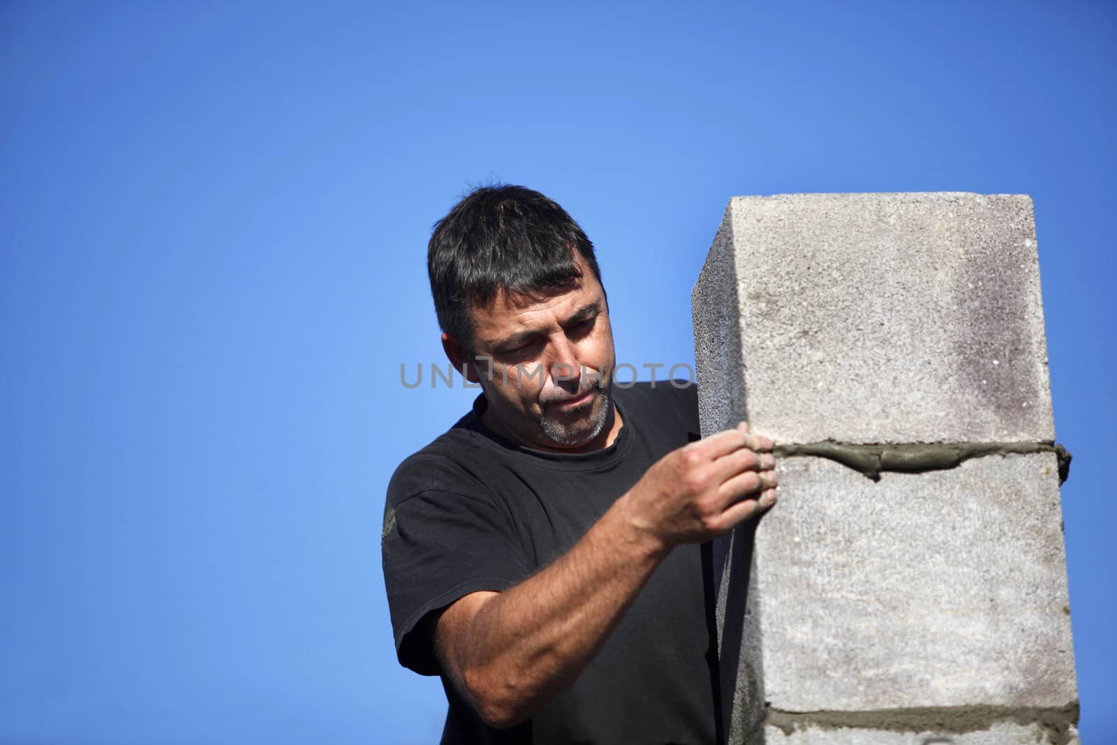 mason erecting a stone block wall by phovoir