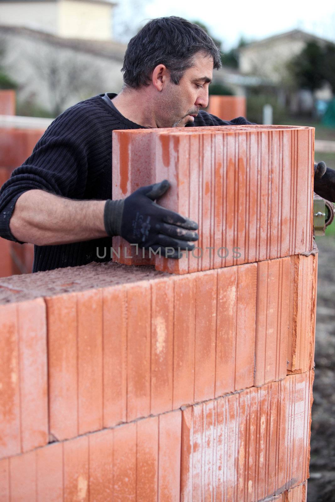 Mason placing brick on unfinished wall by phovoir