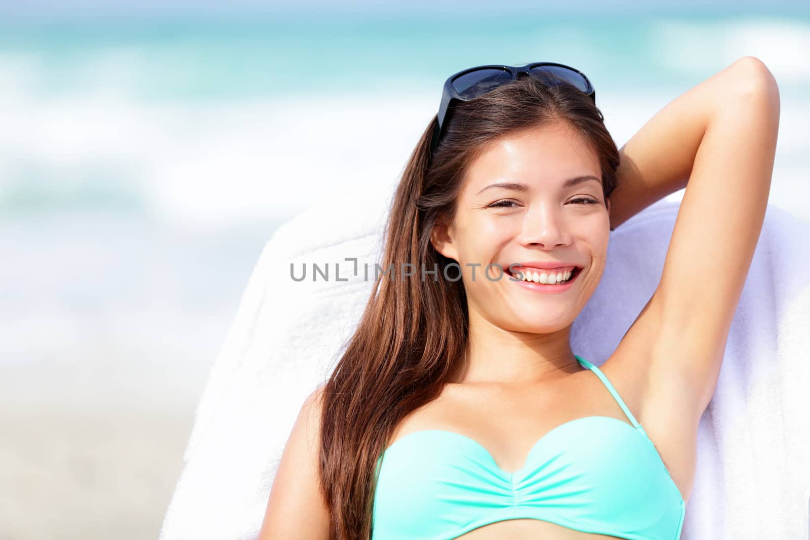 Vacation woman relaxing on sunbed on beach in bikini smiling happy looking at camera. Beautiful young multiracial Caucasian / Asian Chinese enjoying summer holidays in the sun.