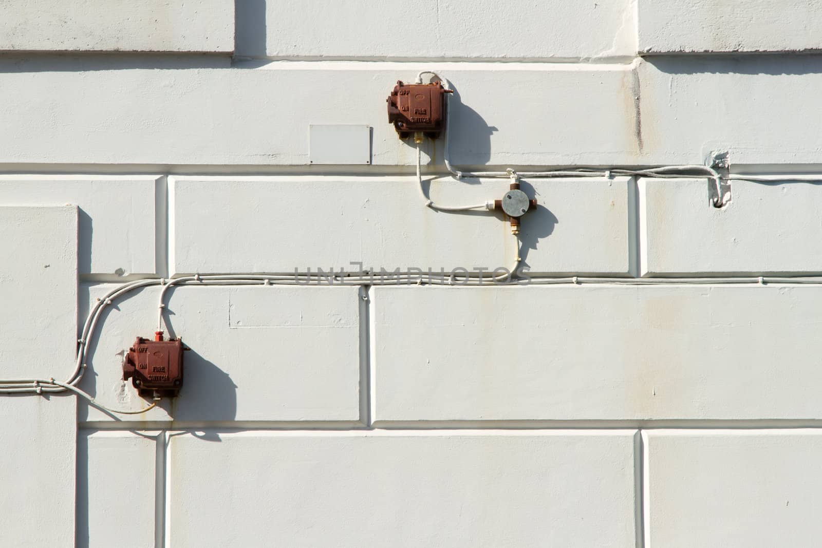 Old outdoor fire switch boxes with cables and a junction box on an external wall with patterned render.