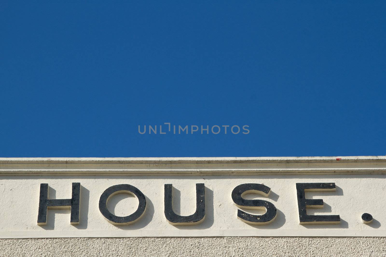 A wall with pebble dash and render with the word 'HOUSE.' on it, against a blue sky.