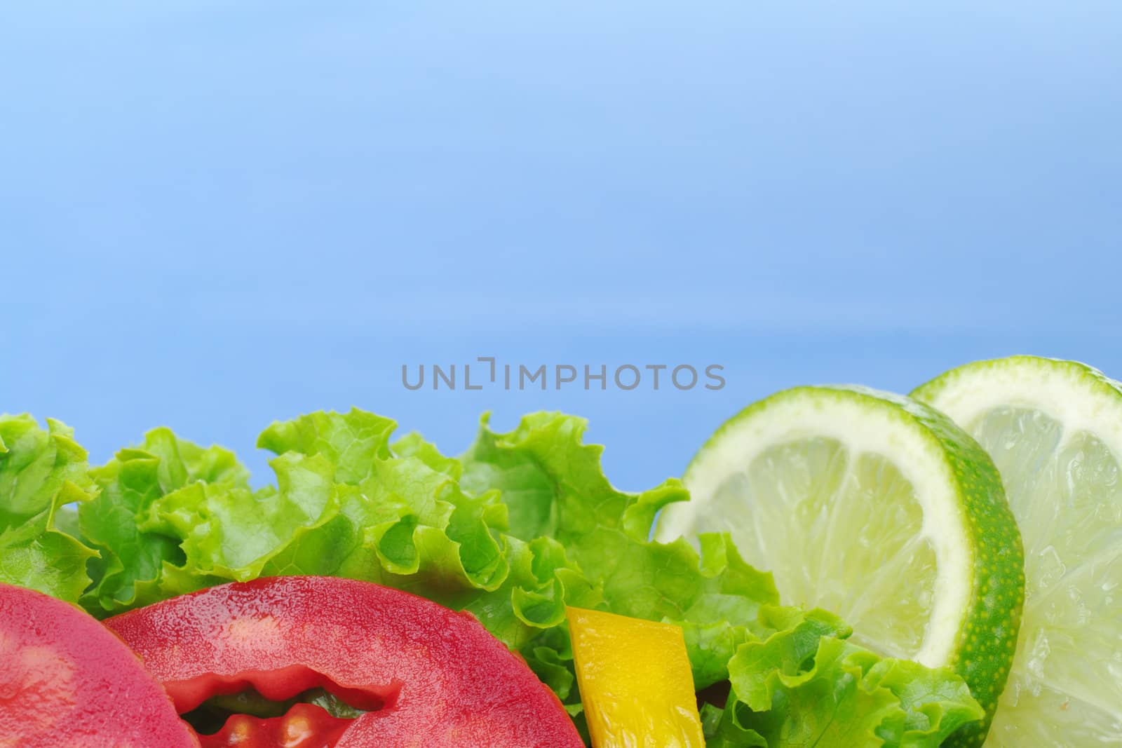 Lettuce, tomato slices, yellow bell pepper and lime slices on blue background (Selective Focus) 