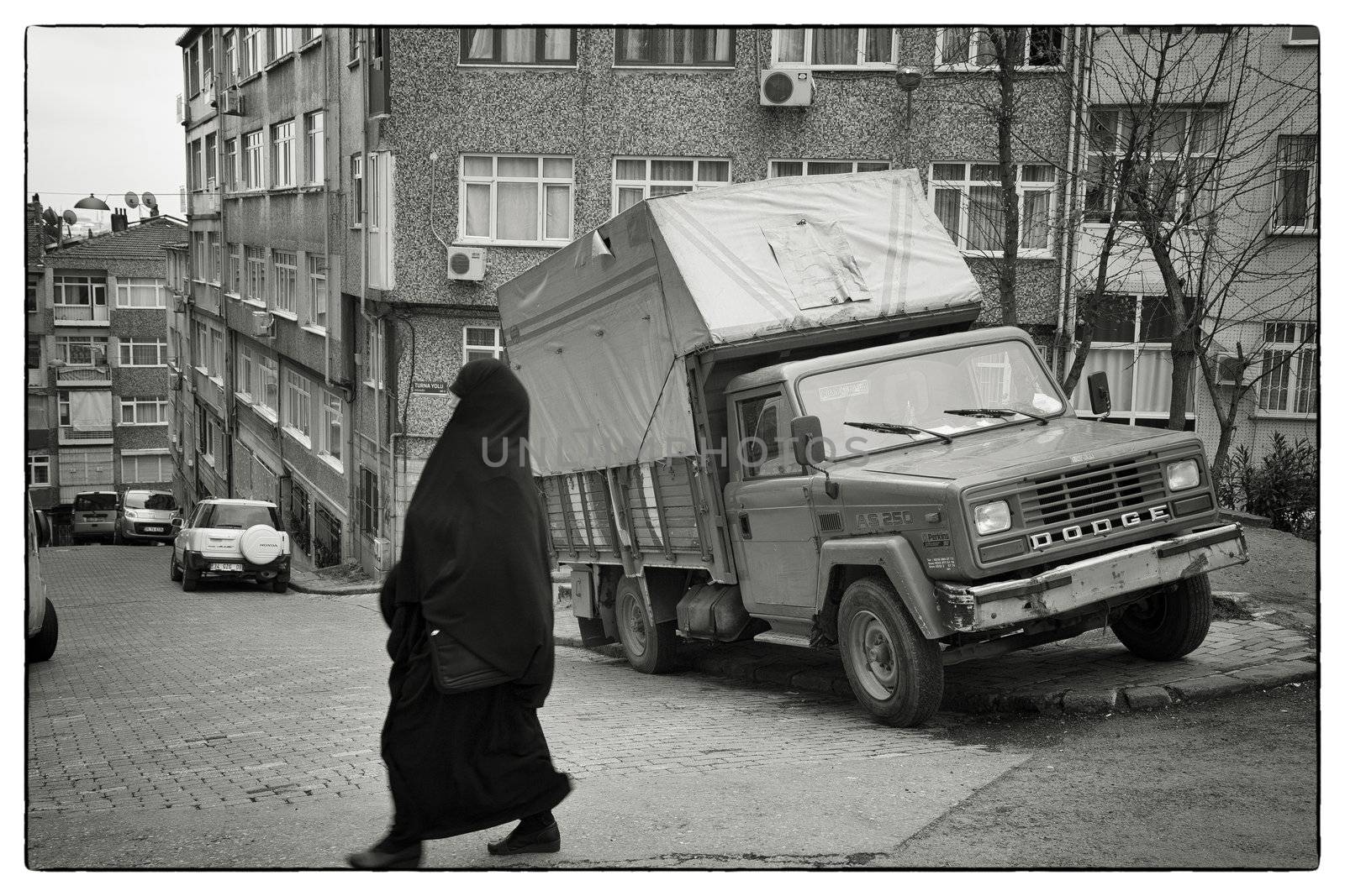 REAL LIFE ISTANBUL, ISTANBUL, TURKEY, APRIL 17, 2012: Typical housing area in the elder part of Istanbul, Turkey. Elderly muslim woman passing a parked truck. Intentional motion blur.