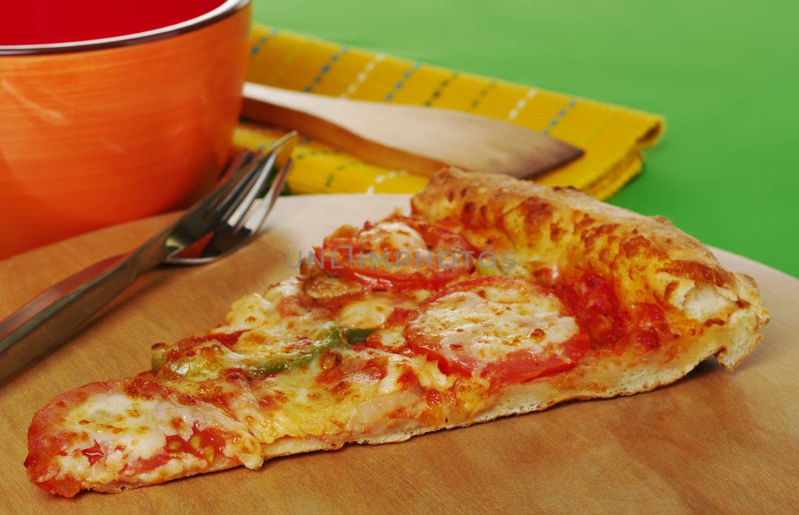 A slice of a pizza on wooden board with cutlery, bowl and table mat (Selective Focus)