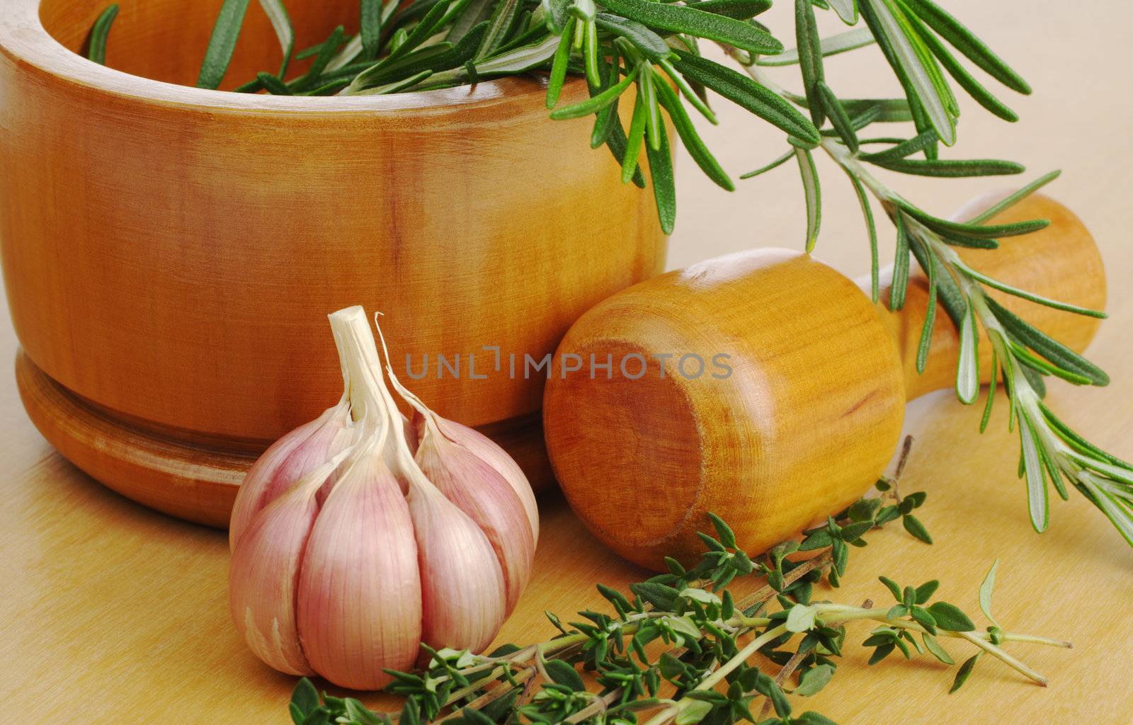 Wooden mortar on wooden board with garlic, rosemary and thyme (Selective Focus)