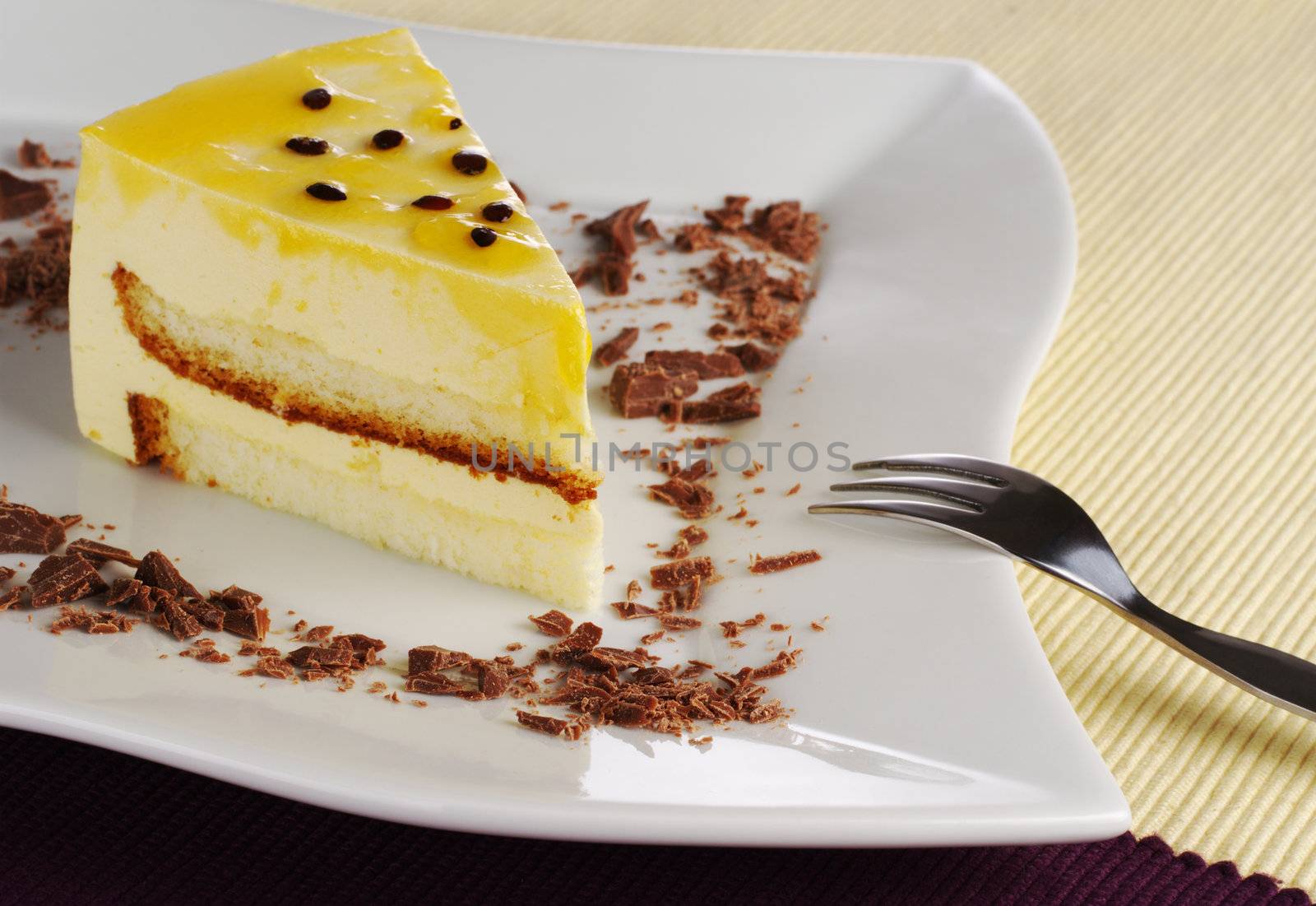 A piece of passionfruit cake with chocolate shavings on white plate with fork (Selective Focus)