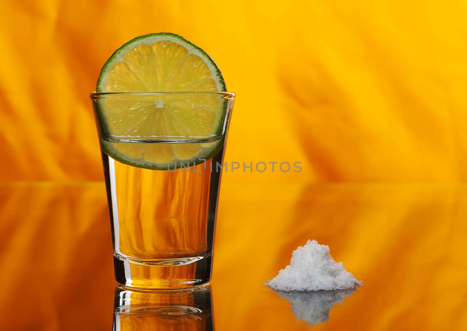 Tequila shot with a slice of lime in the glass and a pile of salt by the side on orange background (Selective Focus)