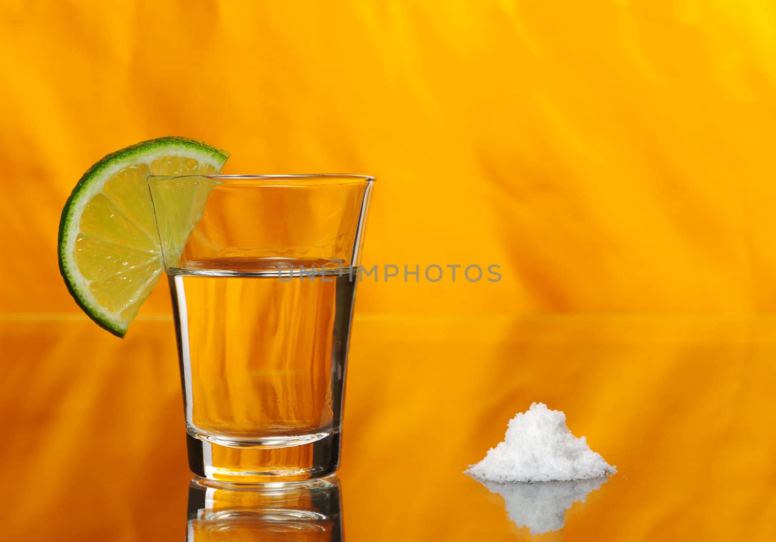 Tequila shot with a half a slice of lime on the glass and a pile of salt by the side on orange background (Selective Focus)