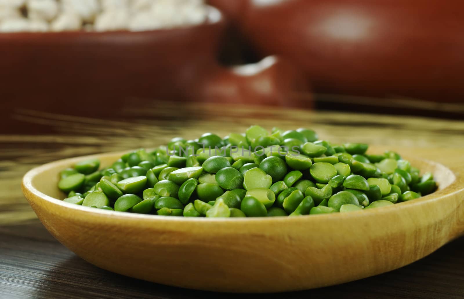 Dried green peas on wooden spoon with crop and bowls in the background (Selective Focus, Focus on the green peas)