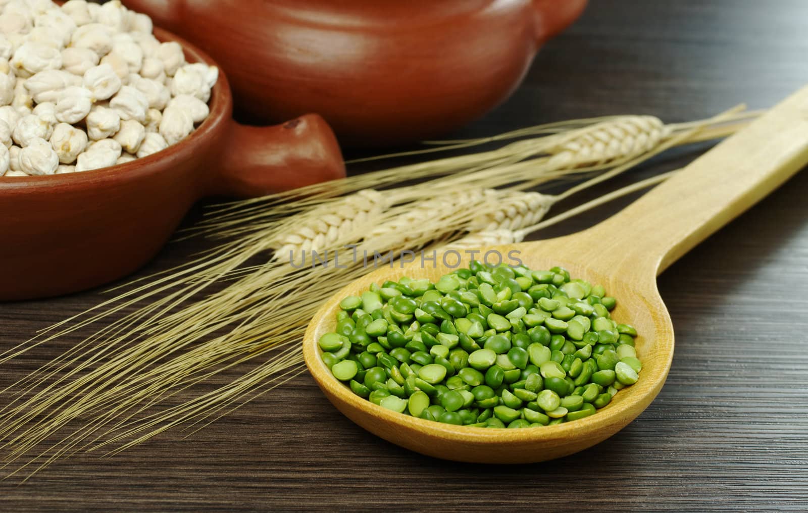 Dried green peas on wooden spoon with crop and bowls in the background (Selective Focus, Focus on the green peas and the front of the spoon)