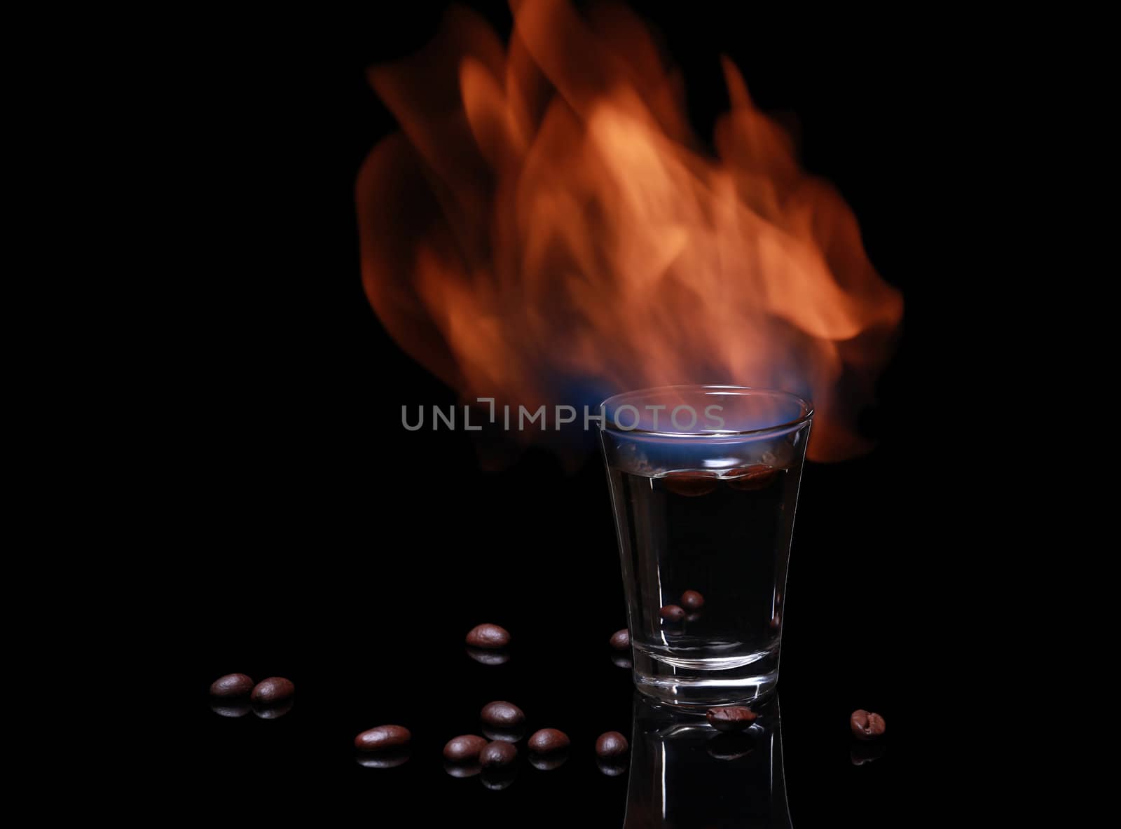 Flaming Sambuca surrounded by coffee beans photographed on black 