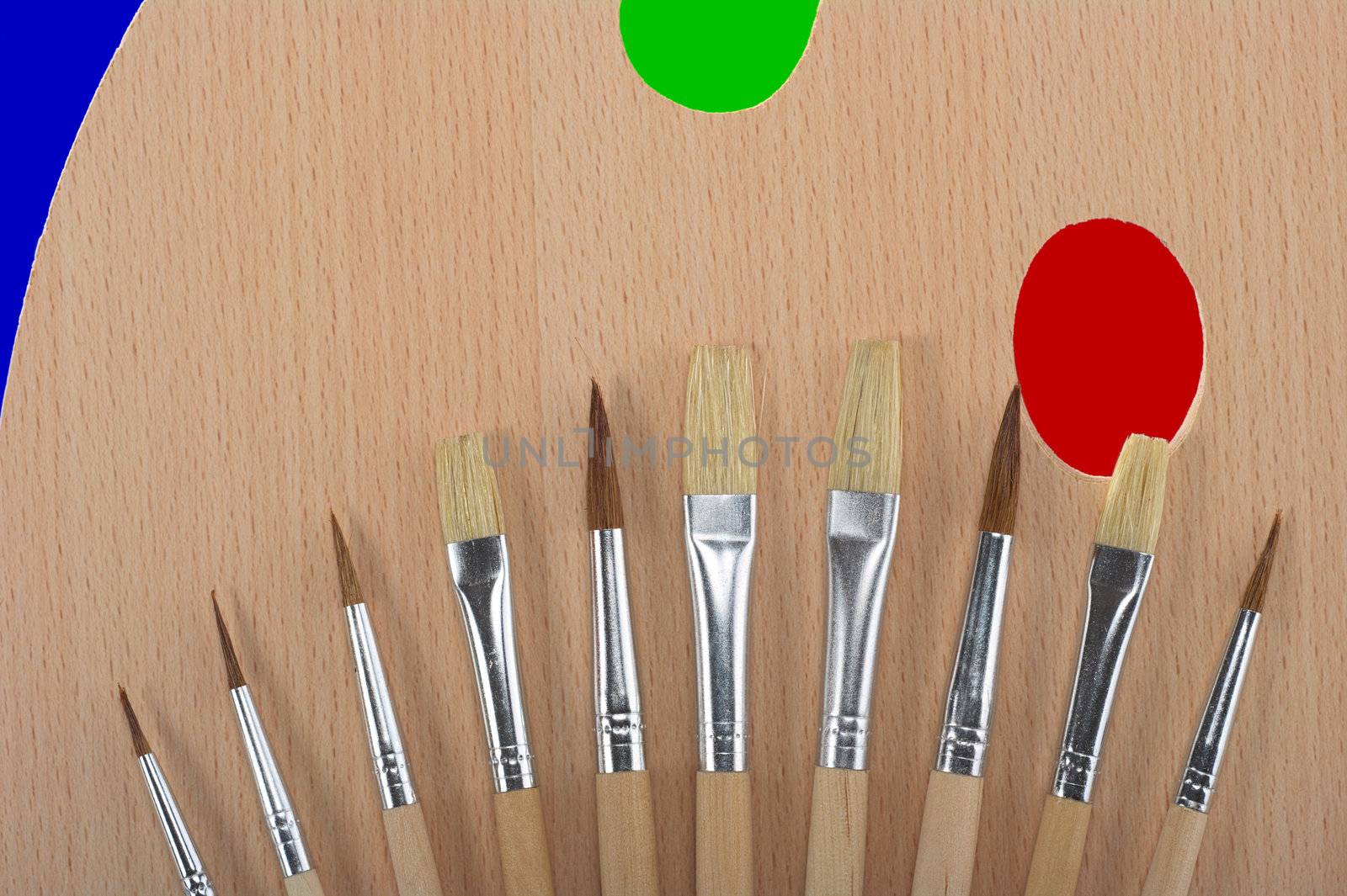 A painter's palette with many different sized brushes and different color spots 
