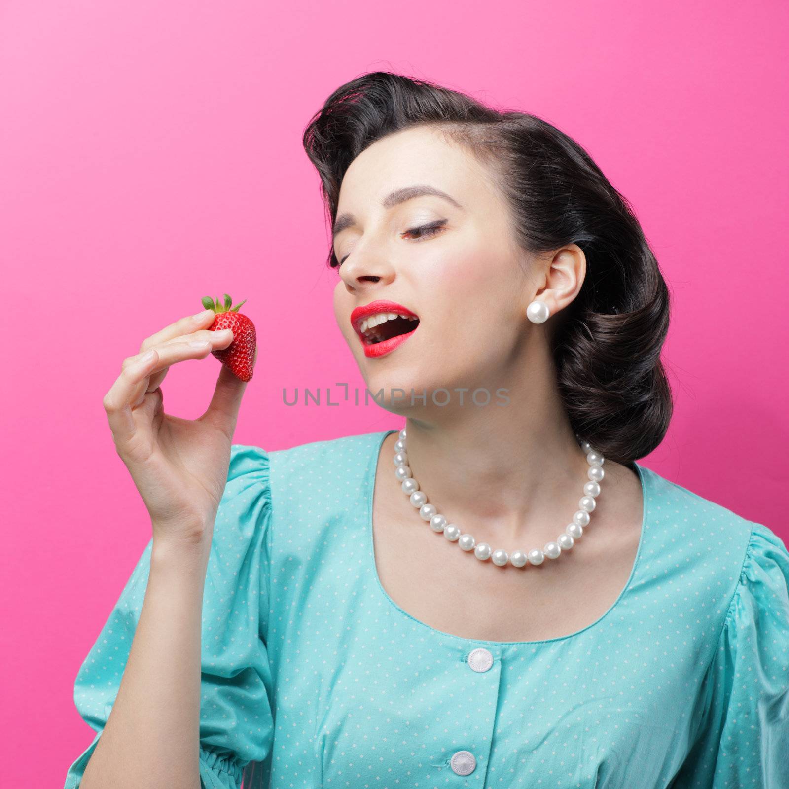 Sensual woman with a red strawberry on pink background