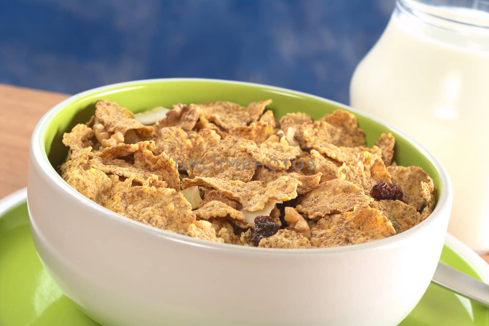 Wholewheat cereal with dried fruit, raisin and walnut in bowl and with milk in the back (Selective Focus, Focus one third into the bowl) 