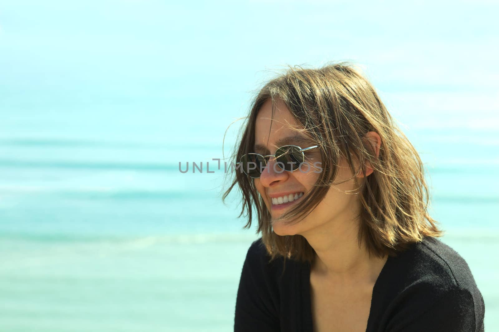 Portrait of a smiling young woman in sunglasses on the coast (Selective Focus, Focus on the left side of the face)