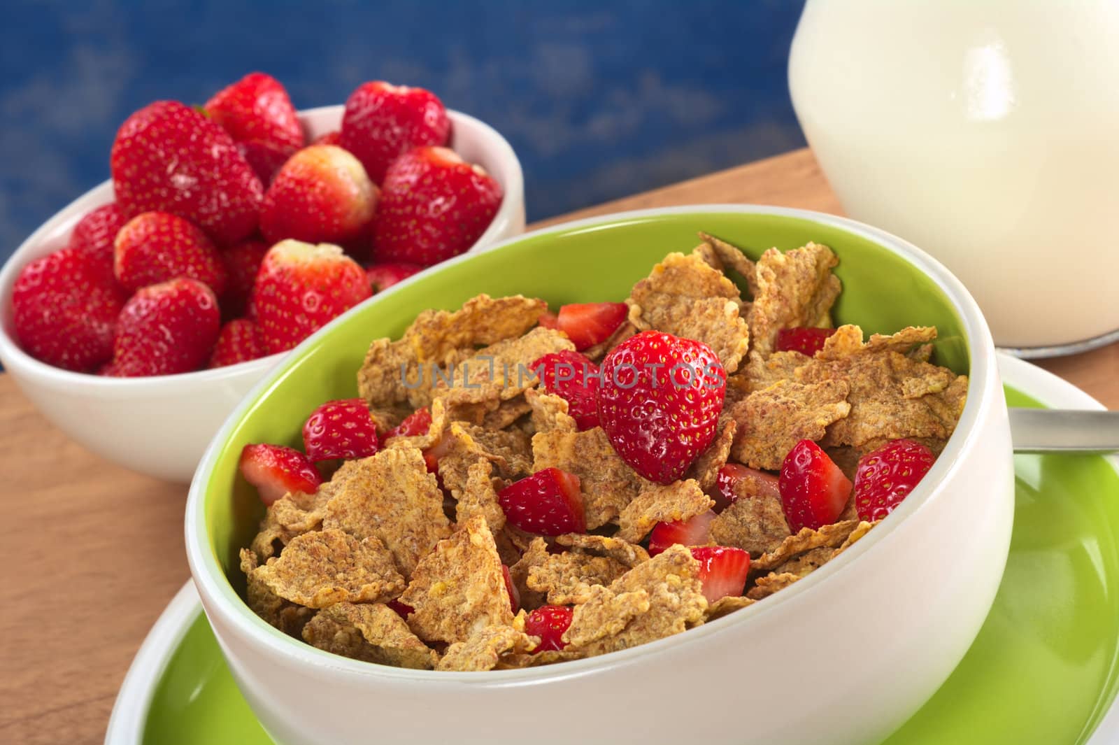 Wholewheat cereal with fresh strawberries in bowl with strawberries and milk in the back (Selective Focus, Focus on the strawberry in the middle) 