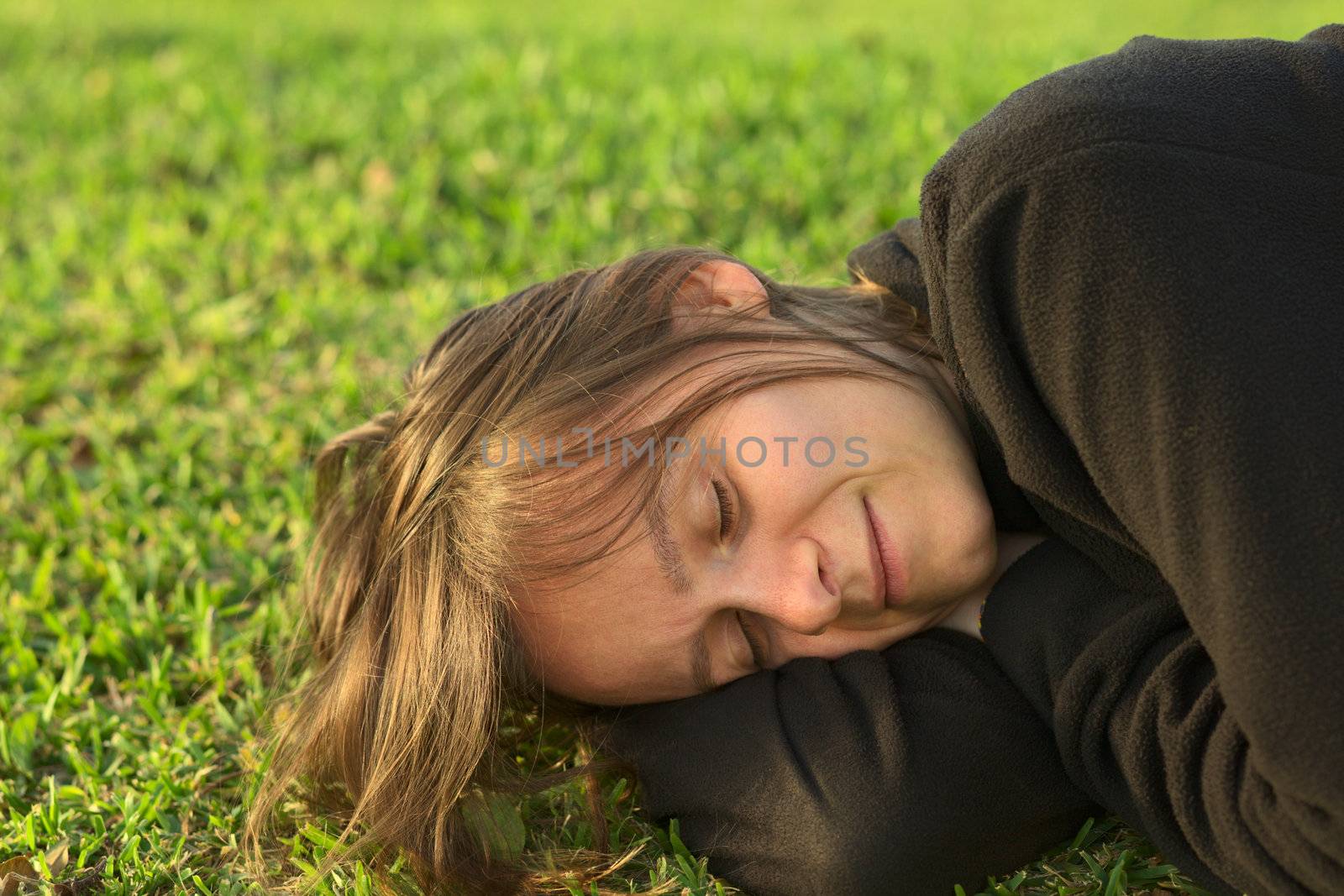Young Caucasian woman sleeping on grass in a park lit by the evening light (Selective Focus, Focus on the left eye)