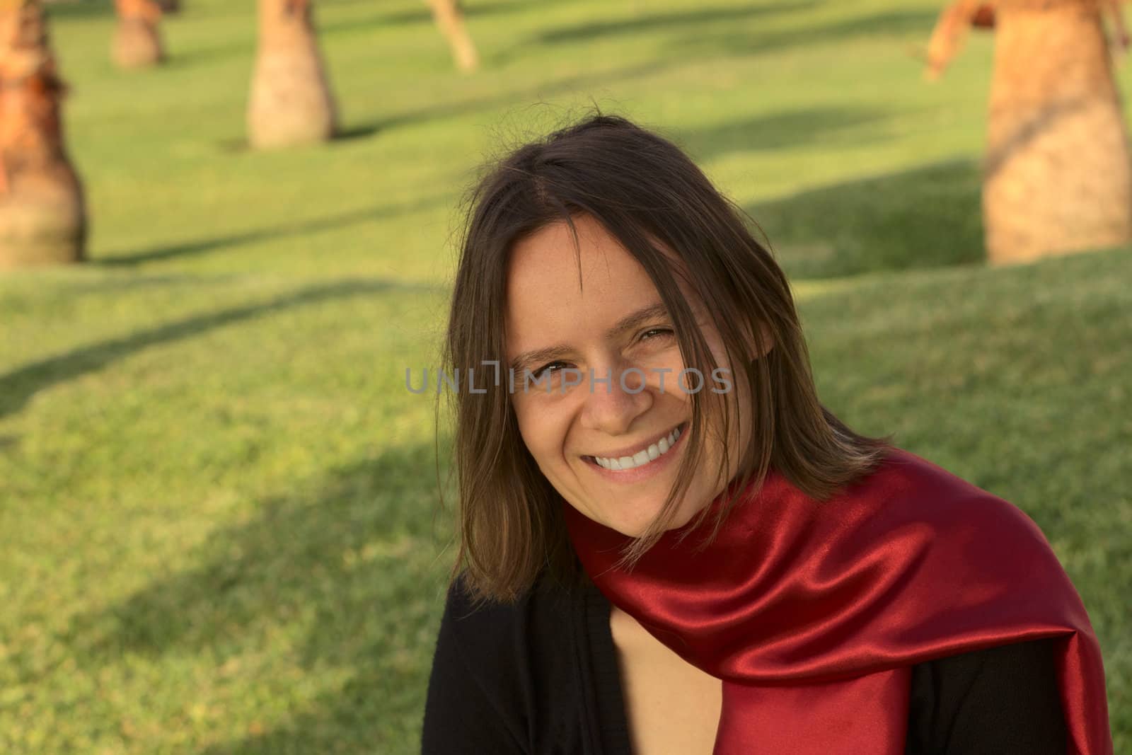 Portrait of a smiling young woman with a red scarf in a park in the evening light (Selective Focus, Focus on the face of the woman) 