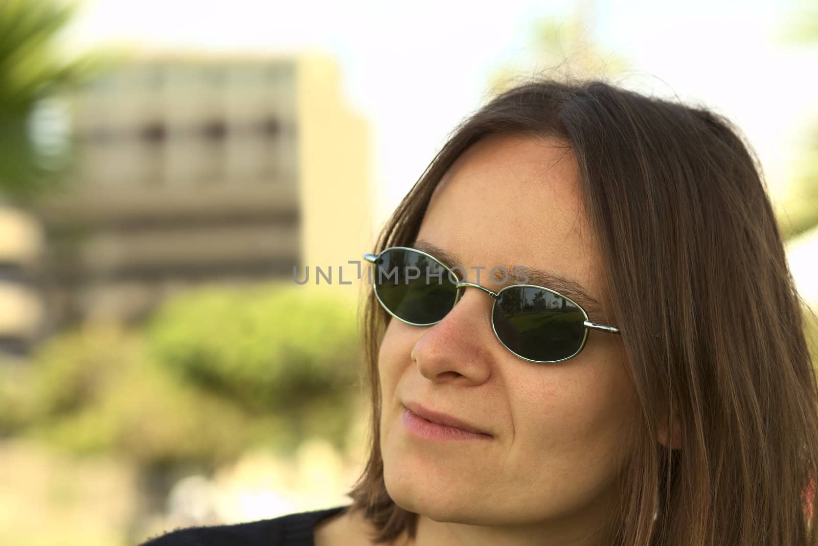 Portrait of a young woman in sunglasses with a building and trees in the background (Selective Focus, Focus on the left eyebrow and sunglasses)