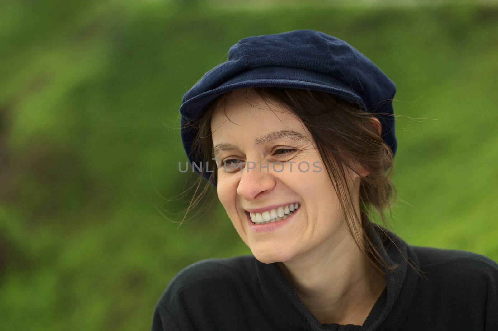 Smiling young Caucasian woman with a blue gatsby cap in a park (Selective Focus, Focus on the left eye)