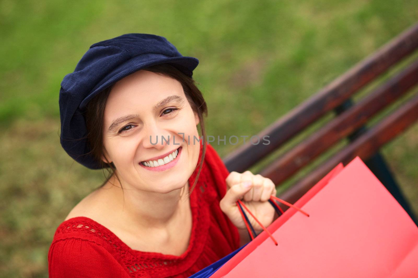 Happy young Caucasian woman with shopping bags sitting on a bench (Selective Focus, Focus on the eyes)