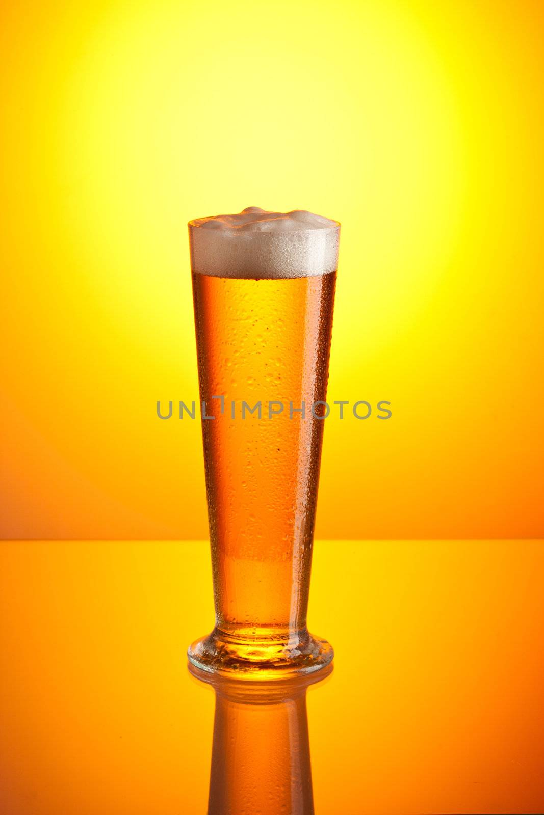 glass of foamy beer over golden background