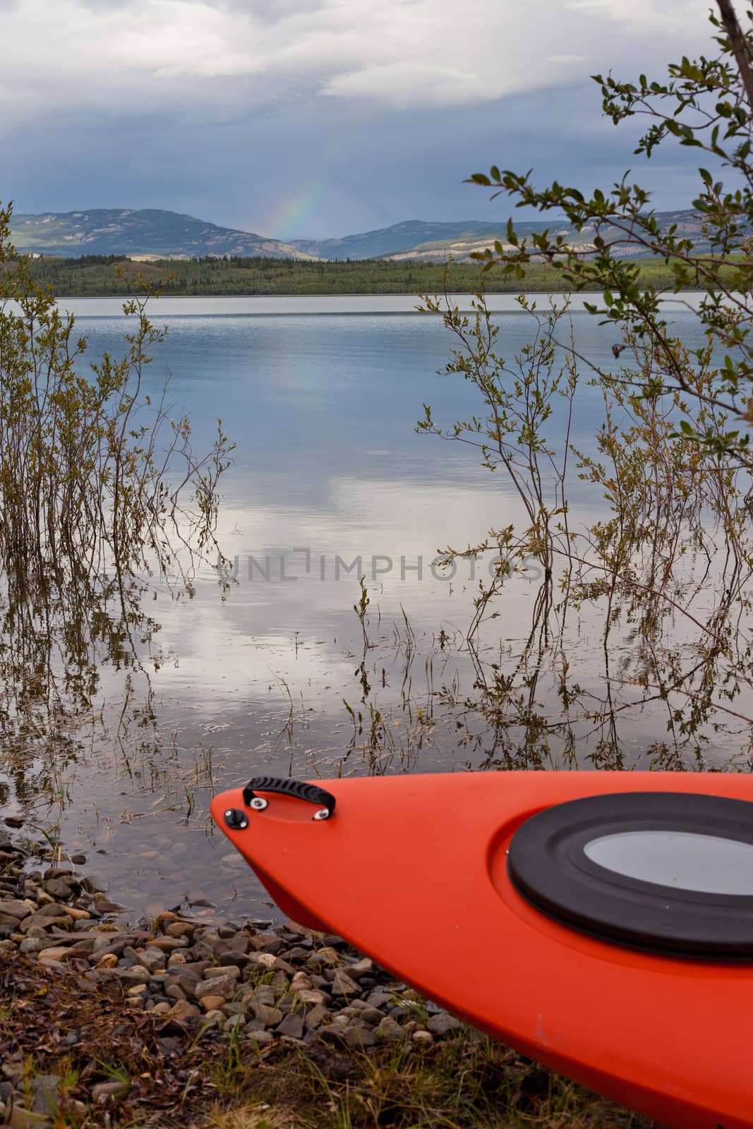 Kayak beached on the shore alongside a tranquil lake with a mountain range in the distance