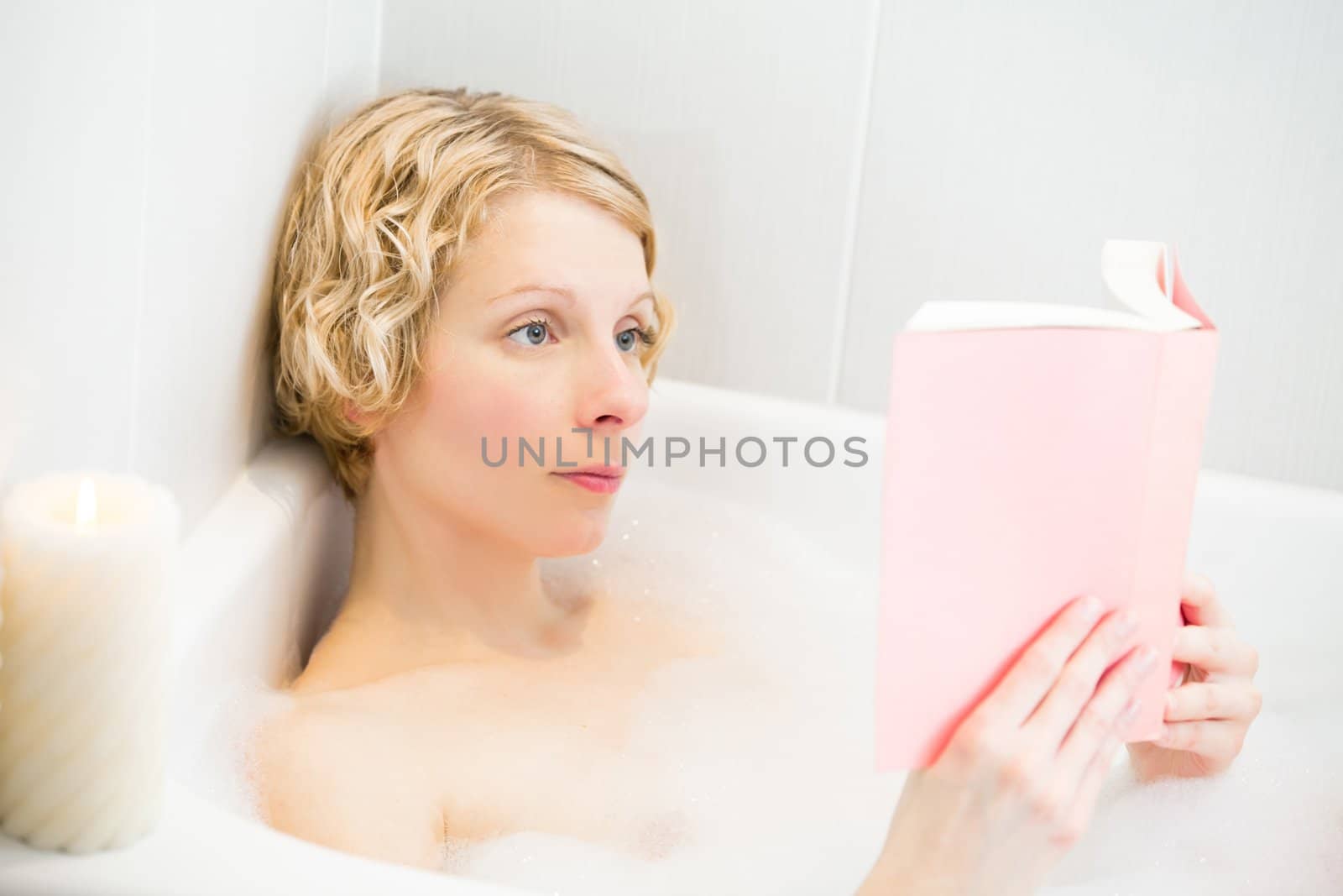 Young woman relaxing in the bath and reading a book by aetb